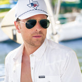 Man wearing a white cap and sunglasses with boats in the background