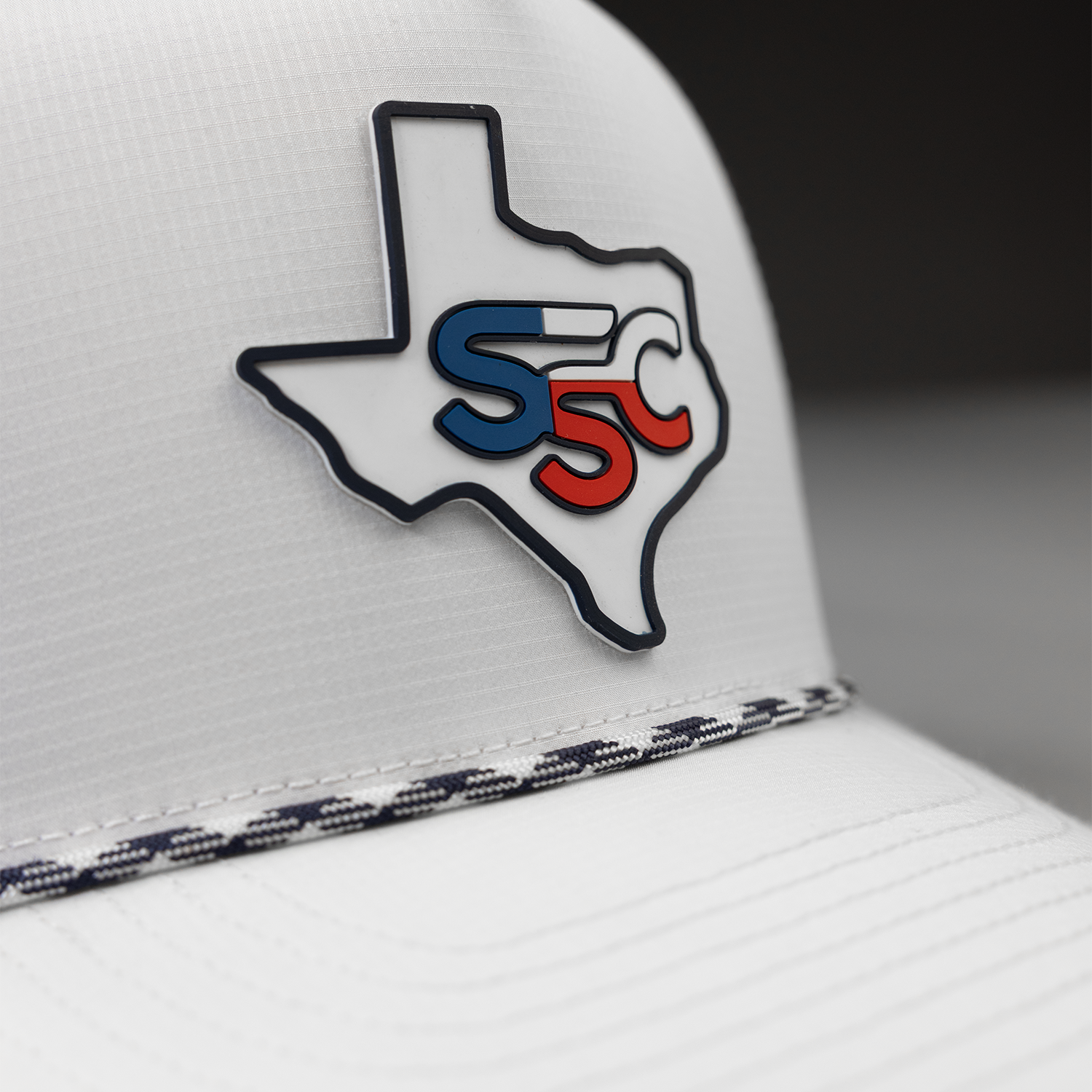 White cap with Texas-shaped logo featuring 'SSC' in blue and red on a blurred background