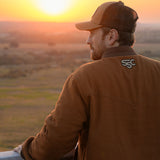 Eric Nelsen wearing "The Stockshow" bomber jacket, back towards the camera, looking out over a fence looking at the sunset. 