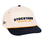 Stockyard Supply Co two tone rope hat with block lettering, cream top with navy bill. Monogram logo on the side