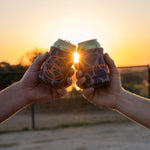 Two friends doing a "cheers" displaying both sides of the coozie. One displaying the duckster logo, the other displaying the primary logo.