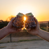 Two friends doing a "cheers" displaying both sides of the coozie. One displaying the duckster logo, the other displaying the primary logo.