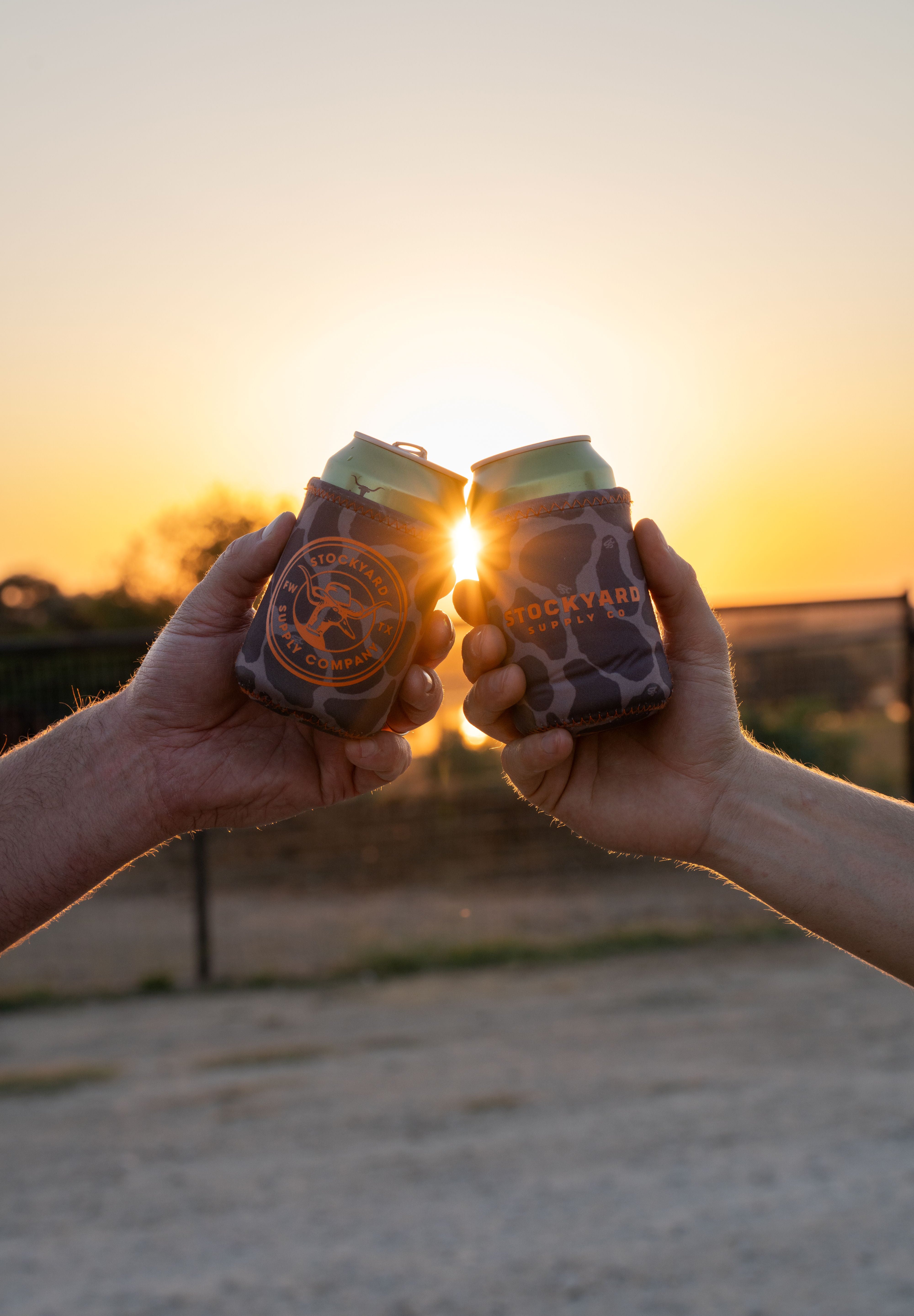 Two friends doing a "cheers" displaying both sides of the coozie. One displaying the duckster logo, the other displaying the primary logo.