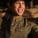 JP Guana sitting down wearing a black cowboy hat and the long sleeve olive green performance pearl snap from Stockyard Supply Co