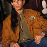 JP Guana sitting down wearing a black cowboy hat wearing a Stockyard Supply Co Olive pearl snap shirt under "The Stockshow" Canvas Bomber Jacket.