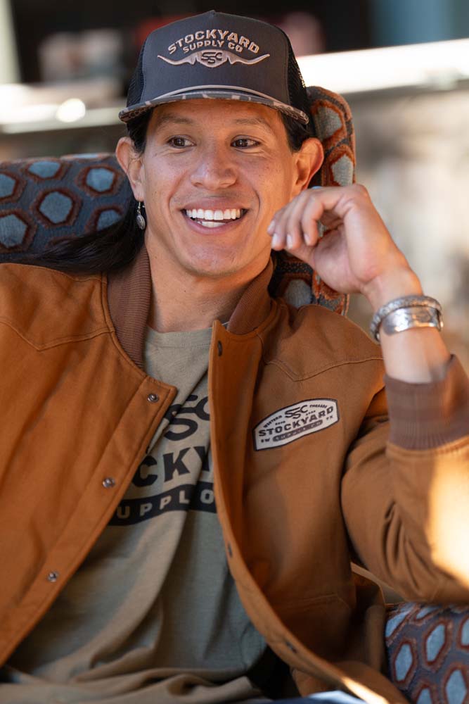 JP Guana sitting down wearing a Stockyard Supply Co "Commander" hat wearing a Stockyard Supply Co Olive T-Shirt under "The Stockshow" Canvas Bomber Jacket.