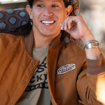 JP Guana sitting down wearing a Stockyard Supply Co "Commander" hat wearing a Stockyard Supply Co Olive T-Shirt under "The Stockshow" Canvas Bomber Jacket.