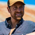 Eric Nelsen wearing the Everyday Jack Trucker Hat - Coyote and Brown colored with a Stockyard Supply Co Faded Navy Pearl Snap long sleeve button down leaning against truck.