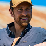 Eric Nelsen wearing the Everyday Jack Trucker Hat - Coyote and Brown colored with a Stockyard Supply Co Faded Navy Pearl Snap long sleeve button down leaning against truck.