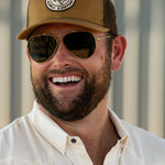 Ryan Dukes laughing wearing the Everyday Jack Trucker Hat, Brown and Coyote colored with aviator sunglasses. He is wearing the Stockyard Supply Co cream performance pearl snap button down.