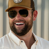 Ryan Dukes laughing wearing the Everyday Jack Trucker Hat, Brown and Coyote colored with aviator sunglasses. He is wearing the Stockyard Supply Co cream performance pearl snap button down.