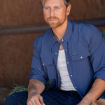 Eric Nelsen wearing Stockyard Supply Co Faded Navy Pearl Snap long sleeve button down sitting on stack of hay