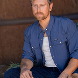 Eric Nelsen wearing Stockyard Supply Co Faded Navy Pearl Snap long sleeve button down sitting on stack of hay