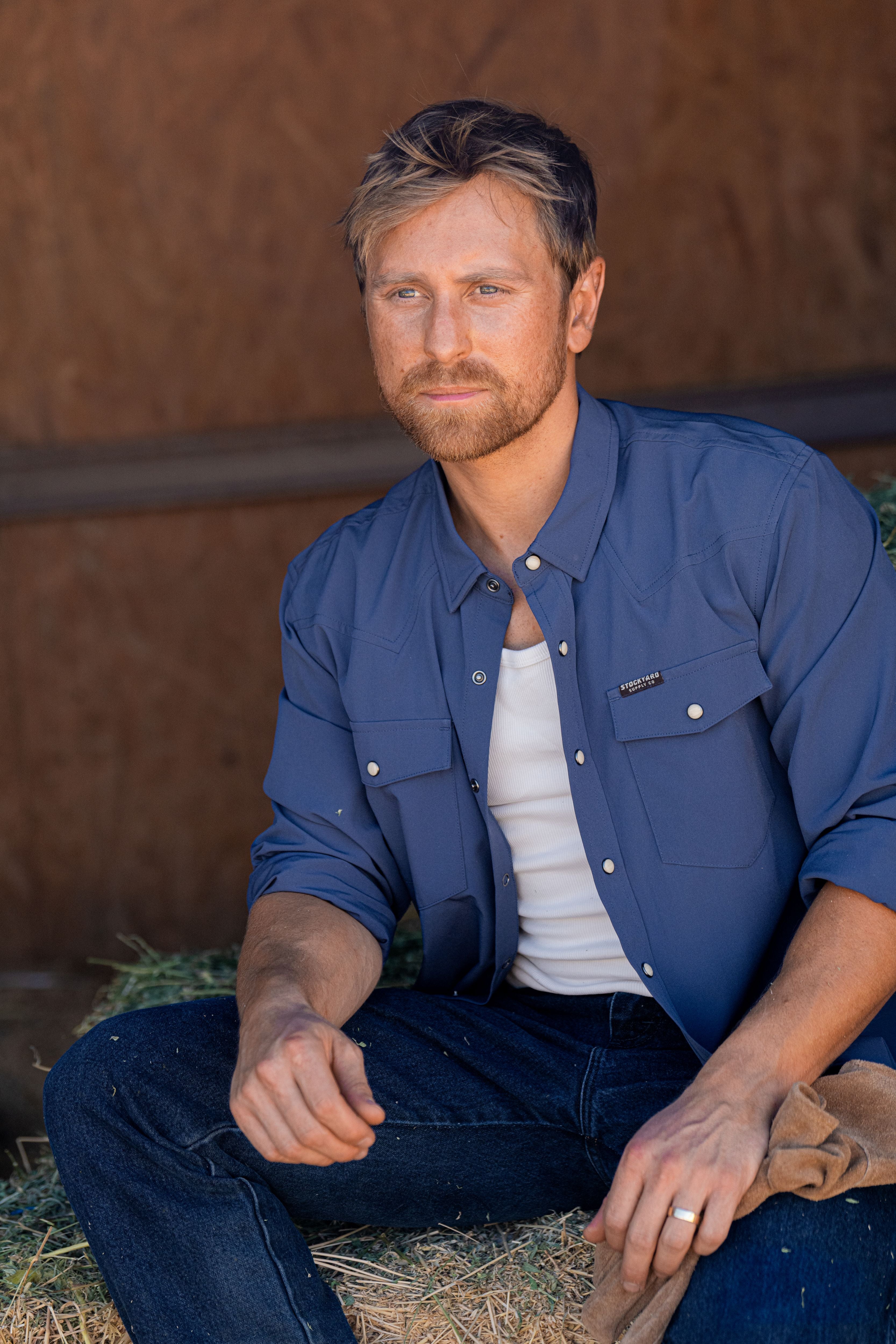 Eric Nelsen wearing Stockyard Supply Co Faded Navy Pearl Snap long sleeve button down sitting on stack of hay