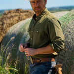 Eric Nelsen wearing a faded olive pearl snap button down shirt leaning against a hay bale