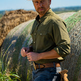 Eric Nelsen wearing a faded olive pearl snap button down shirt leaning against a hay bale