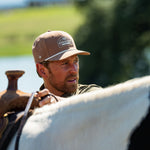 Eric Nelsen wearing the Coyote colored Champion hat and faded olive long sleeve performance pearl snap about to mount a horse.