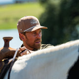 Eric Nelsen wearing the Coyote colored Champion hat and faded olive long sleeve performance pearl snap about to mount a horse.