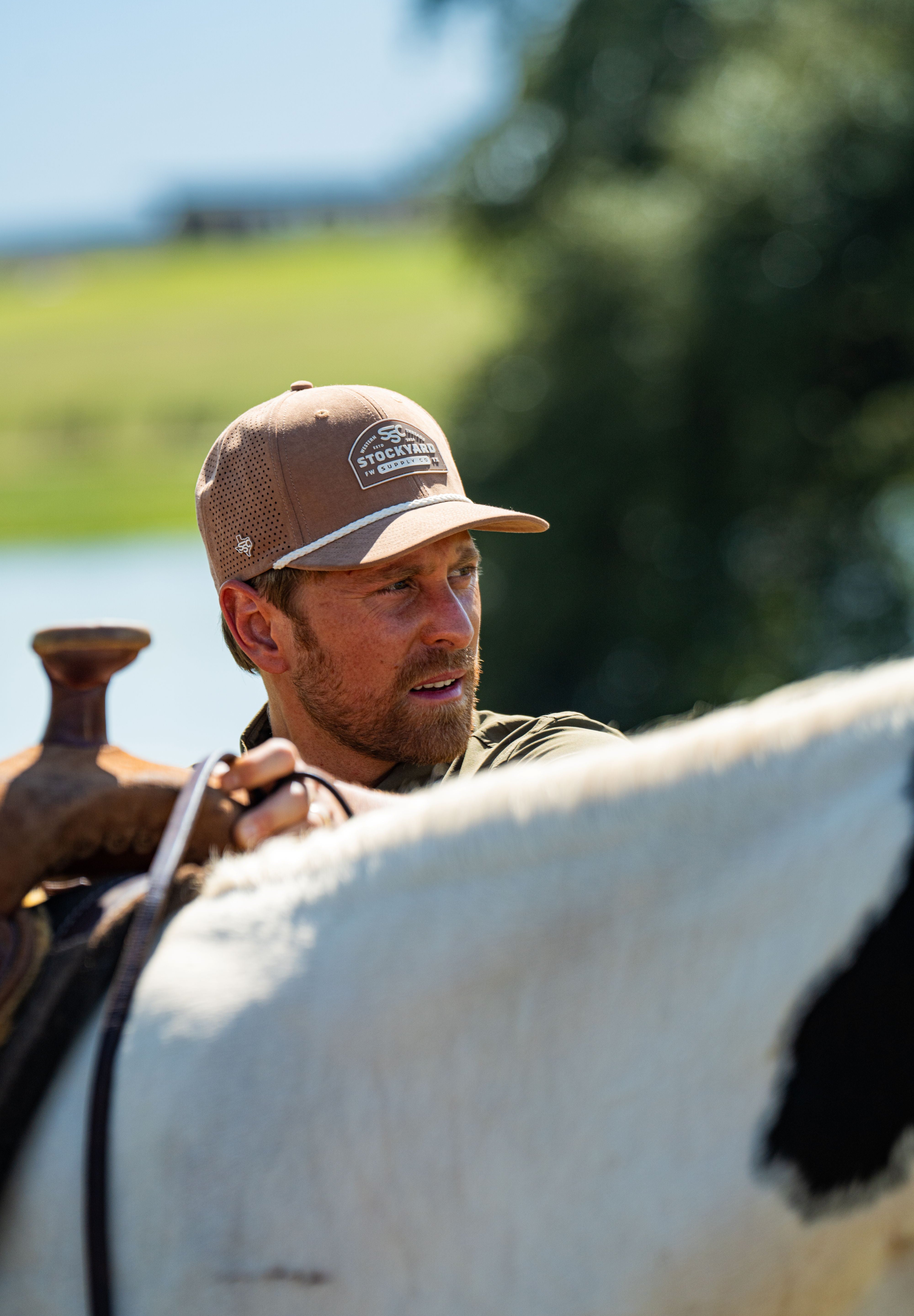 Eric Nelsen wearing the Coyote colored Champion hat and faded olive long sleeve performance pearl snap about to mount a horse.