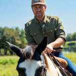 Eric Nelsen wearing the Coyote colored Champion hat and faded olive long sleeve performance pearl snap riding a horse.