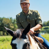 Eric Nelsen wearing the Coyote colored Champion hat and faded olive long sleeve performance pearl snap riding a horse.