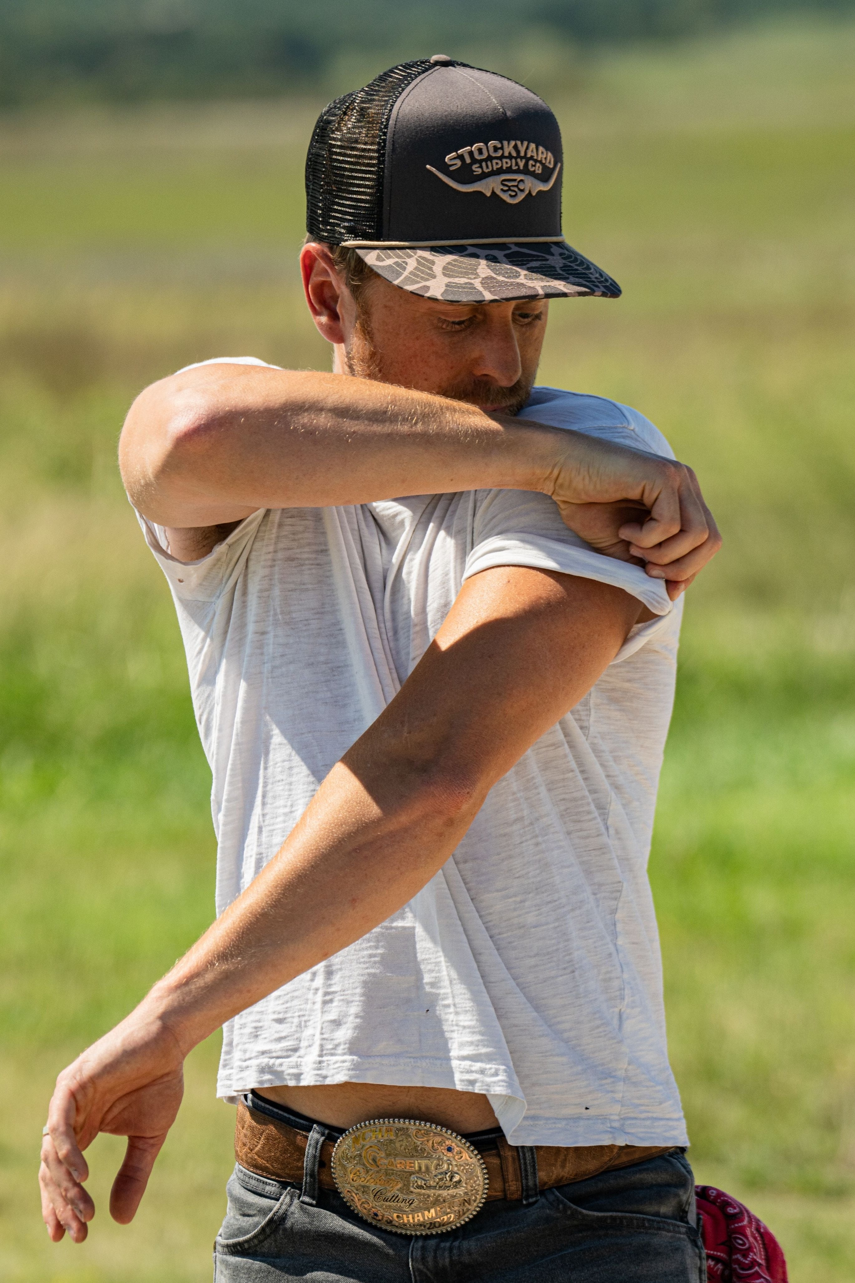 Eric Nelsen wearing a white shirt with the Commander Stockyard Supply Co hat with a black mesh and camo pattern brim rolling up his sleeves.